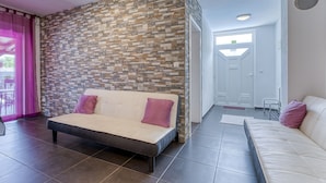 A modern living room with a sofa and a bed, a stone wall, and a view of the outside. - Radmila by Interhome (Krk/Šilo)
