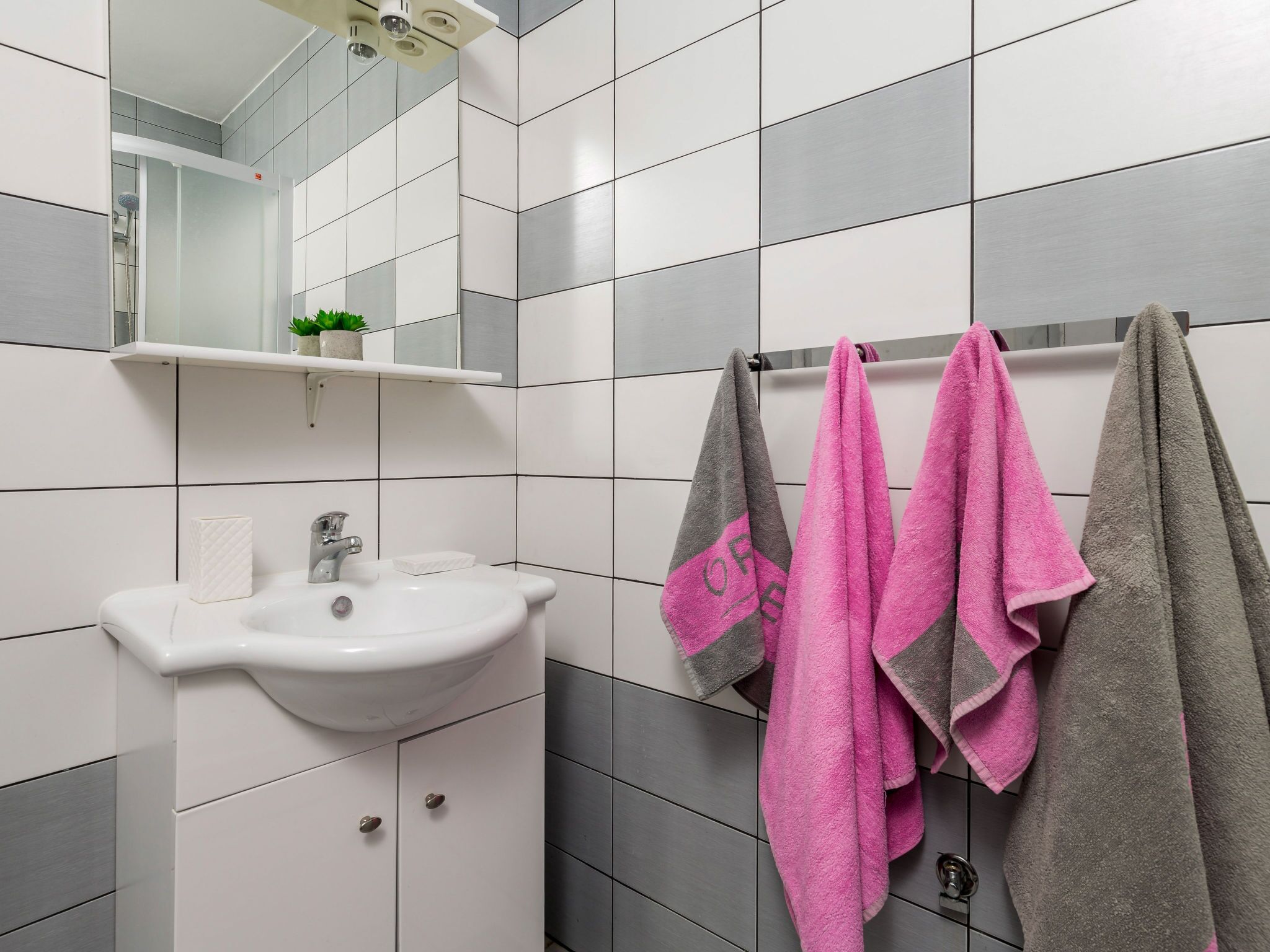 A bathroom with a white sink, mirror, and two towel racks with pink and gray towels.