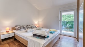 A bedroom with a bed, bedside lamps, a nightstand, and a view of the outdoors through a glass door. - Radmila by Interhome (Krk/Šilo)