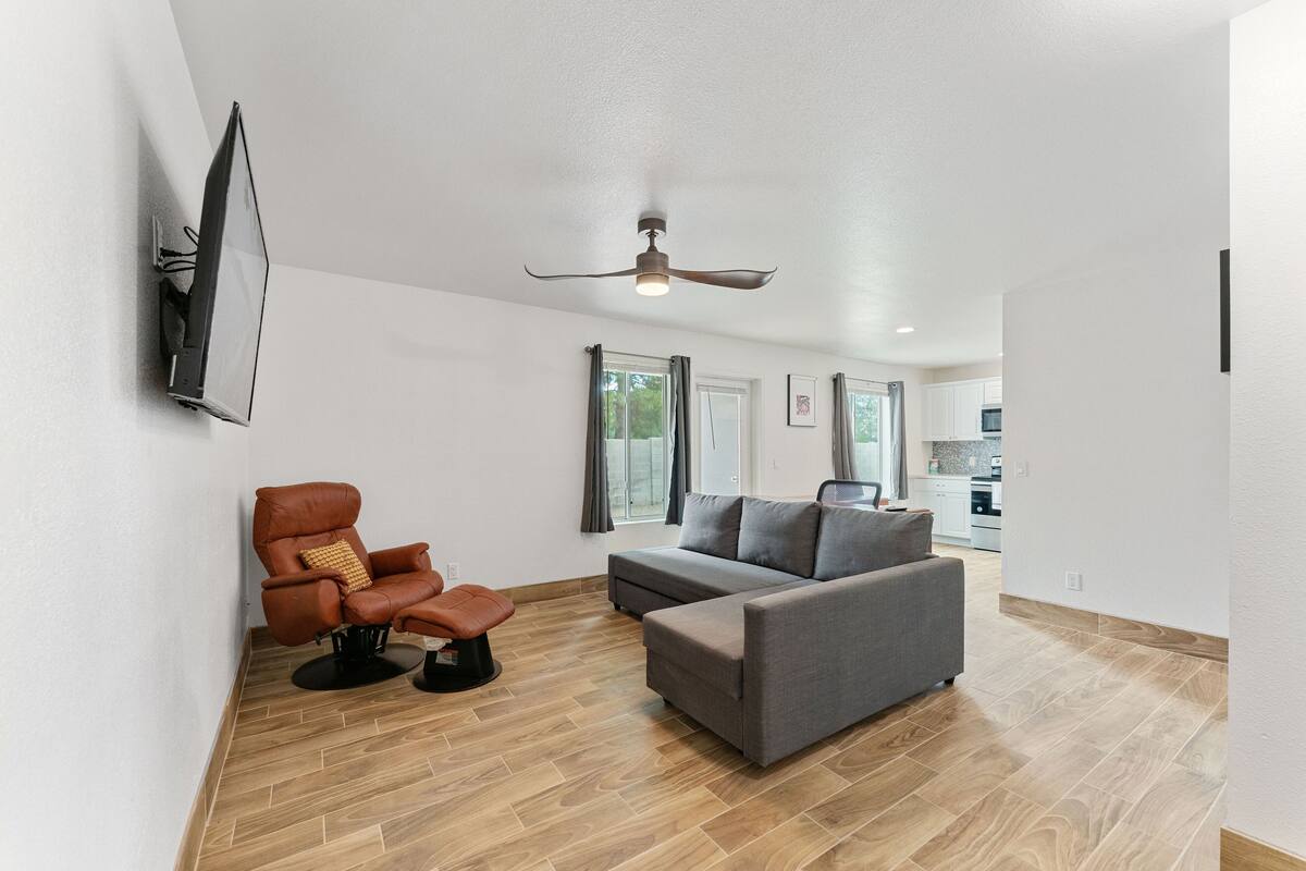 A modern living room with a sofa, a recliner, and a flat-screen TV mounted on the wall.
