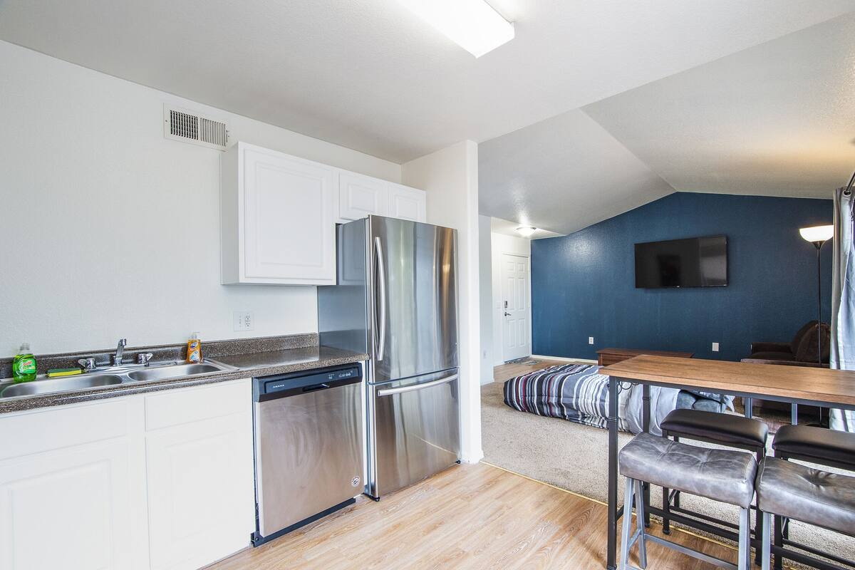 A modern kitchen with stainless steel appliances, white cabinetry, and a wooden dining table with bar stools.