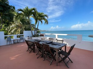 Une terrasse extérieure avec une table et des chaises, donnant sur une plage et l’océan.