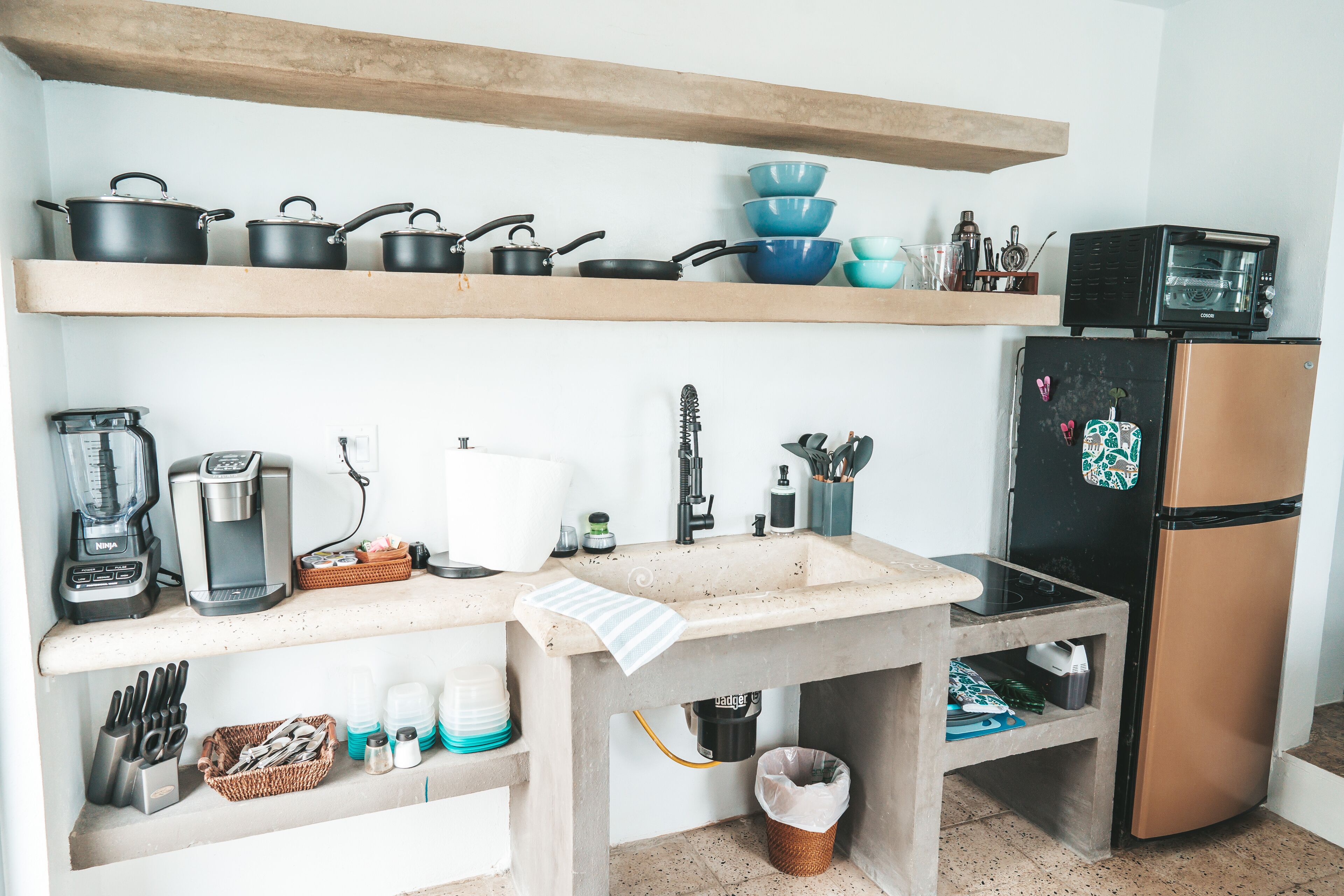 Une cuisine équipée d’un plan de travail en bois, d’un évier, d’une cuisinière, d’un réfrigérateur, ainsi que de divers ustensiles et appareils de cuisine.
