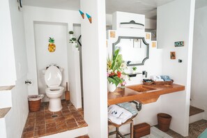 Une salle de bain avec des toilettes blanches, un lavabo avec un miroir et une petite plante.