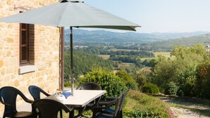 Ein Steinhaus mit Tisch und Stühlen unter einem großen Sonnenschirm mit Blick auf ein Tal.