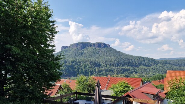 A view of a mountainous landscape with a wooden deck and a red-roofed building. - Vacation in nature - view of the Elbe Sandstone Mountains in Saxon Switzerland (Königstein)