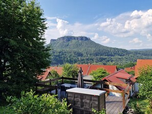 A view of a mountainous landscape with a wooden deck and a red-roofed building. - Nature Vacations—View of the Elbe Sandstone Mountains in Saxon Switzerland   (Königstein)