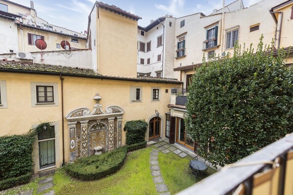 A courtyard with a small garden, a stone pathway, and a building with ornate architectural details.