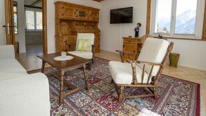 Un salón espacioso con techo de madera, televisor montado en la pared y un gran ventanal con vistas a la montaña.