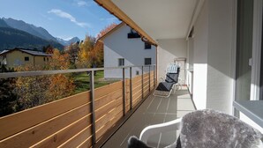 Un balcón con vistas a montañas, baranda de madera y una silla.
