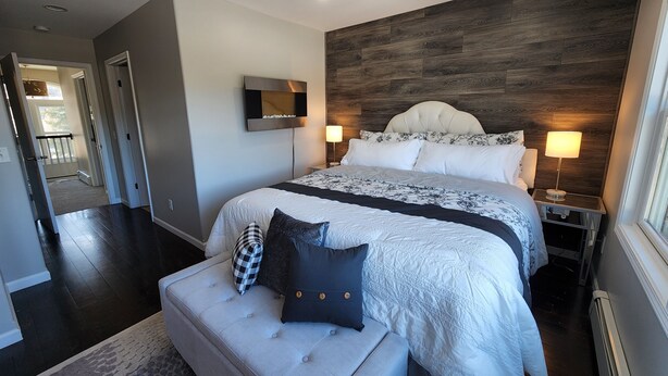 Un dormitorio moderno con una cama grande, un televisor de pantalla plana montado en la pared y una mesita de noche con lámpara.
