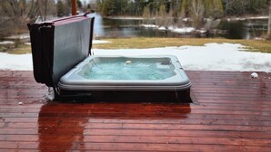 Un jacuzzi en una terraza de madera con un lago y árboles al fondo.