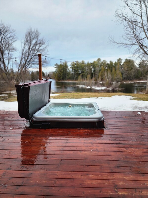 Un jacuzzi en una terraza de madera con un lago y árboles al fondo.