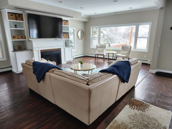 A living room with a beige sectional sofa, a flat-screen TV, a fireplace, and a large window.