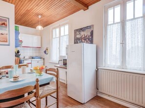 Une cuisine avec un plafond en bois, un réfrigérateur blanc, une table à manger avec des chaises et une fenêtre avec des rideaux.
