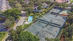 Un quartier résidentiel doté de plusieurs courts de tennis, entouré d’une végétation luxuriante et de maisons.
