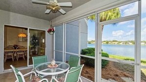 Une terrasse couverte avec une table et des chaises, un ventilateur de plafond et une vue sur un lac.