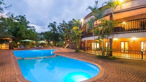 A swimming pool surrounded by a brick patio, with a building featuring balconies and a brick facade in the background. - Greenway woods Self Catering unit no 9, WhiteRiver (White River)