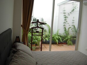 Un dormitorio con cama, un perchero de madera y vistas a un balcón con plantas.