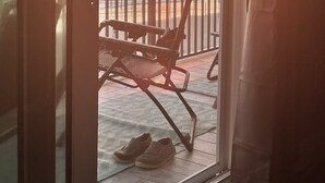 Un balcón con vistas a la puesta de sol sobre el océano, una silla y un par de zapatos en el suelo.