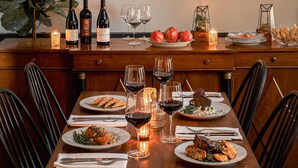 A dining table set with plates of food, wine glasses, and bottles, with a chandelier above and shelves above holding glasses and bottles. - the Alander (Copake)