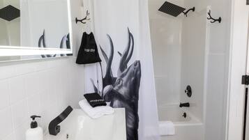A bathroom with a white sink, a mirror, a black towel, and a shower curtain with a black and white design.