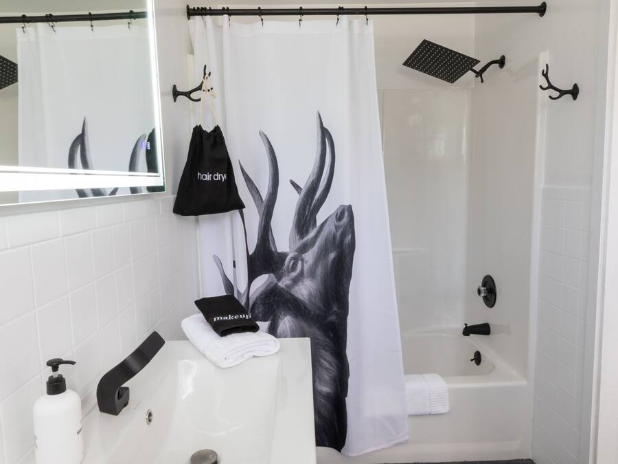 A bathroom with a white sink, a mirror, a black towel, and a shower curtain with a black and white design.