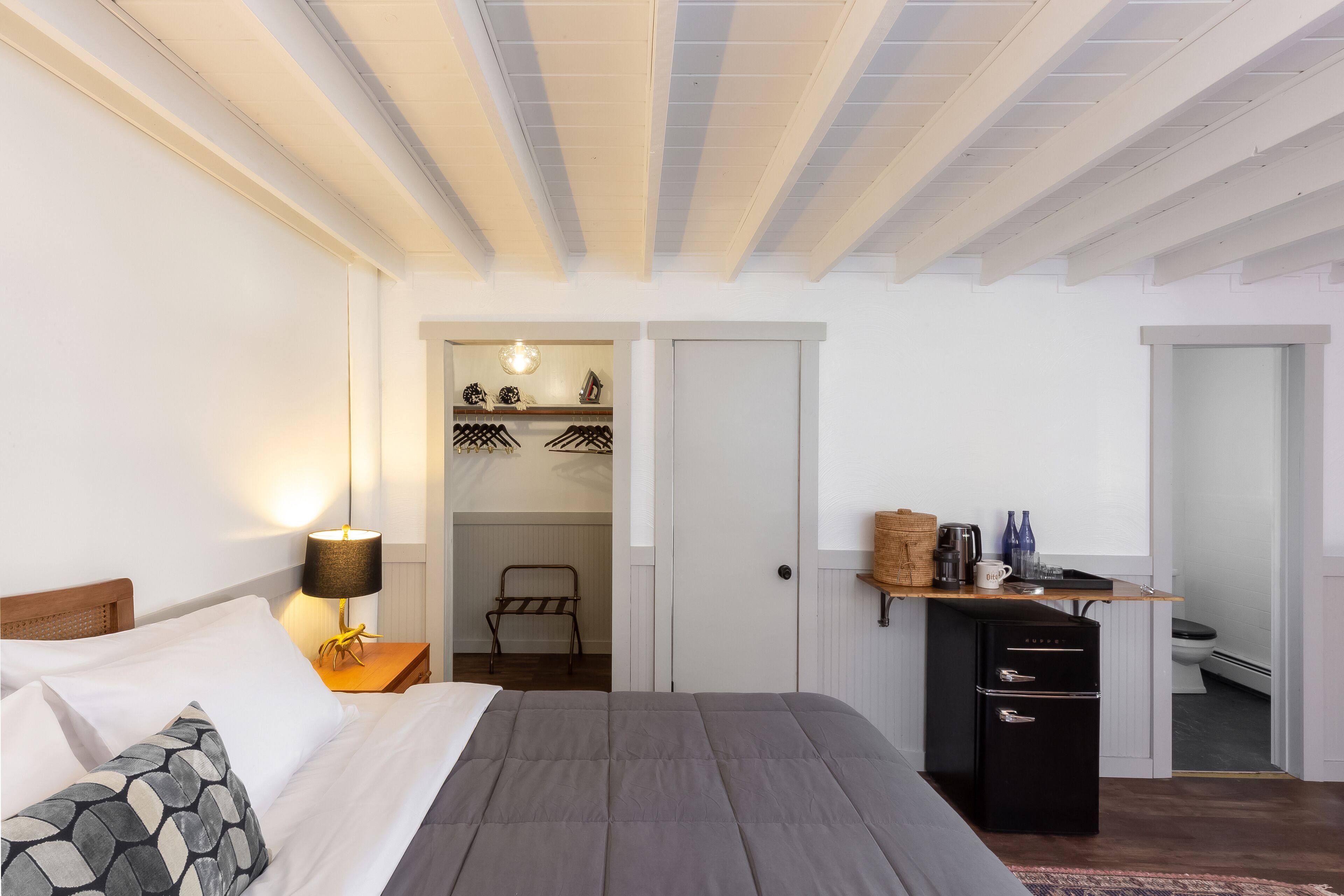 Un dormitorio con cama, lámpara de noche, armario y una pequeña zona de kitchenette.