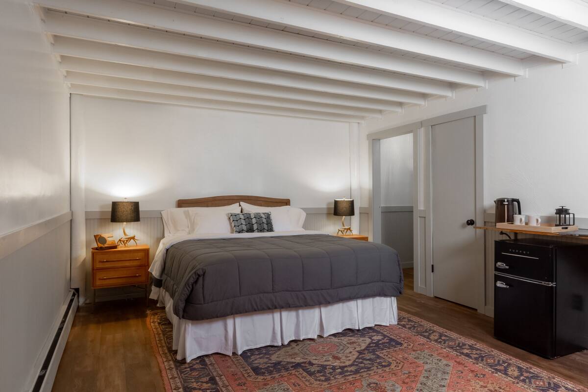 A bedroom with a bed, bedside lamps, a dresser, a desk, and a coffee maker.