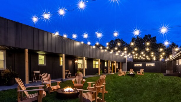 A modern building with a dark exterior, outdoor seating area with wooden chairs, and string lights. - the Alander (Copake)