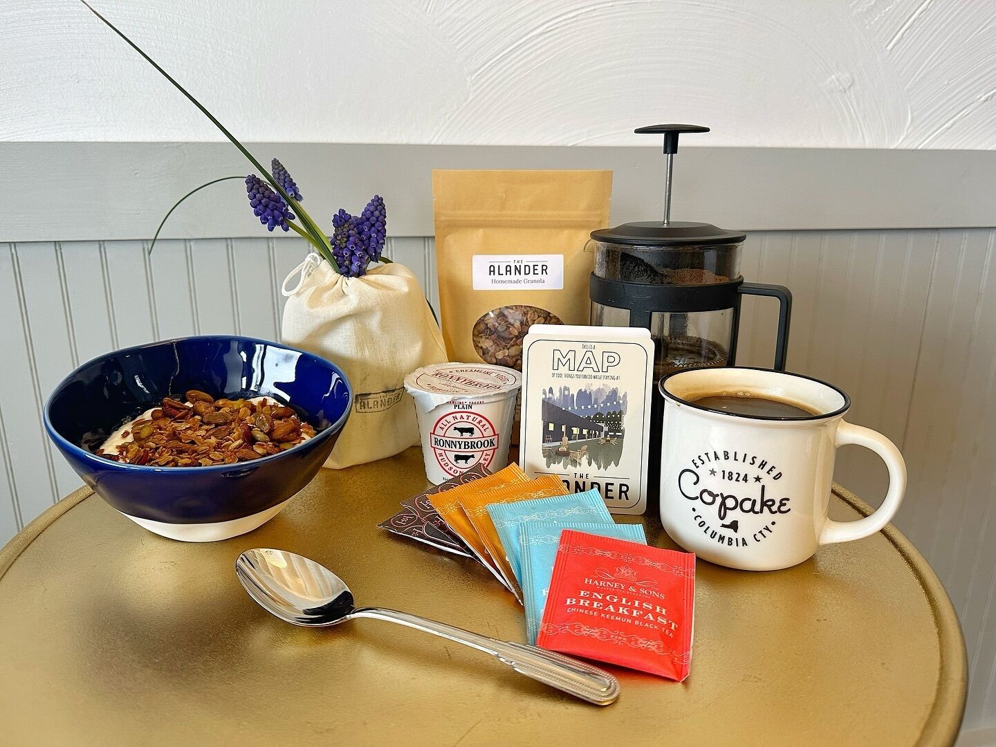 A breakfast setup with a bowl of cereal, a coffee mug, a thermos, a map, and some tea packets.