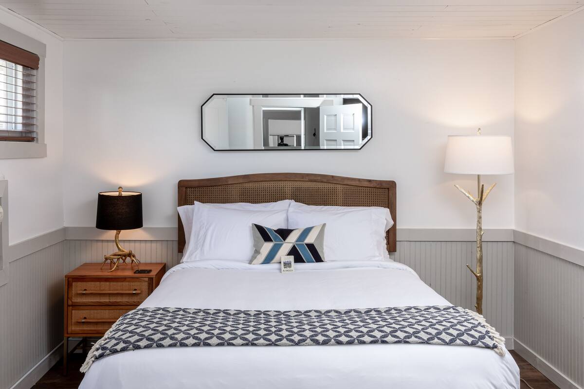 A neatly arranged bedroom with a bed, a bedside table with a lamp, a mirror, and a floor lamp.