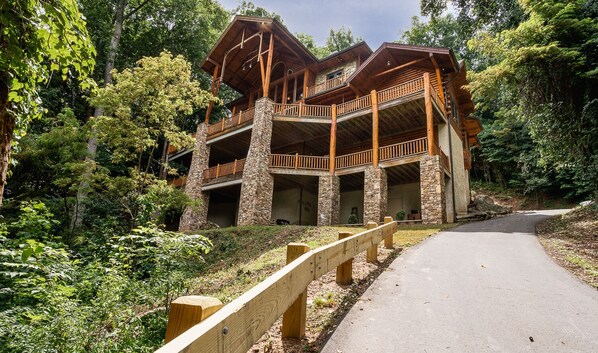 A multi-story log cabin with stone foundations, surrounded by dense forest.