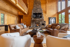Un intérieur chaleureux de chalet en bois, avec une cheminée en pierre, des canapés en cuir et un grand écran de télévision.