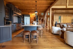 Une cuisine spacieuse dotée d’un îlot central, de tabourets de bar en bois et d’un coin salon confortable avec un canapé et des fauteuils en cuir.