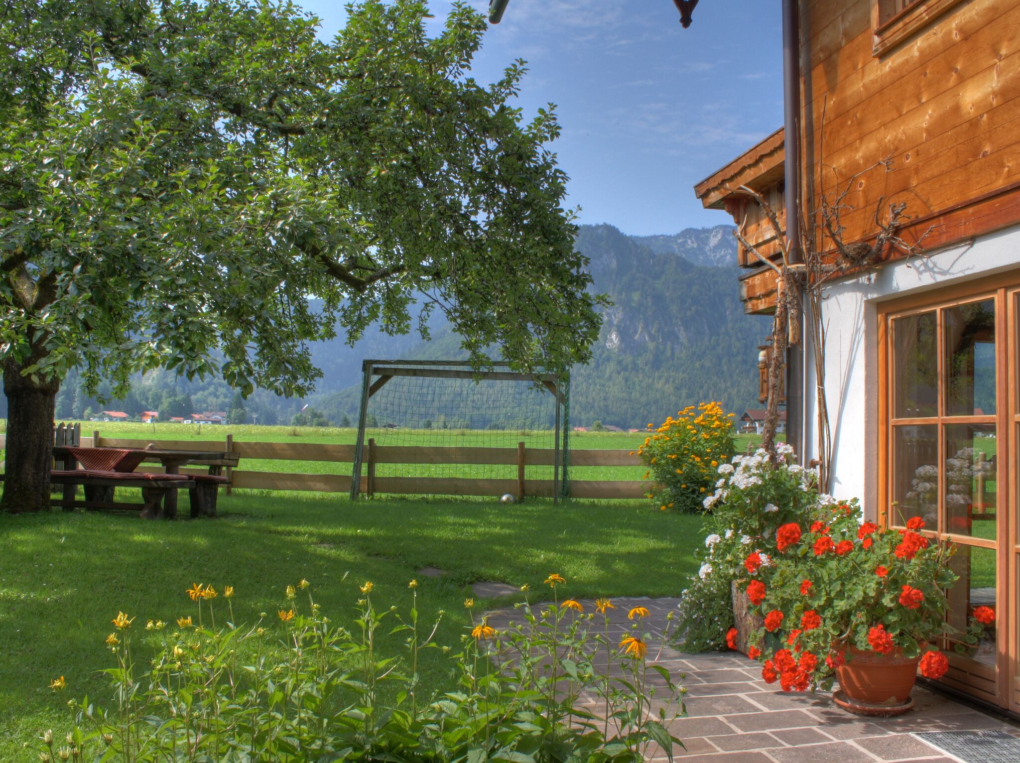 Una casa di legno con un giardino, una panchina e vista sulle montagne.