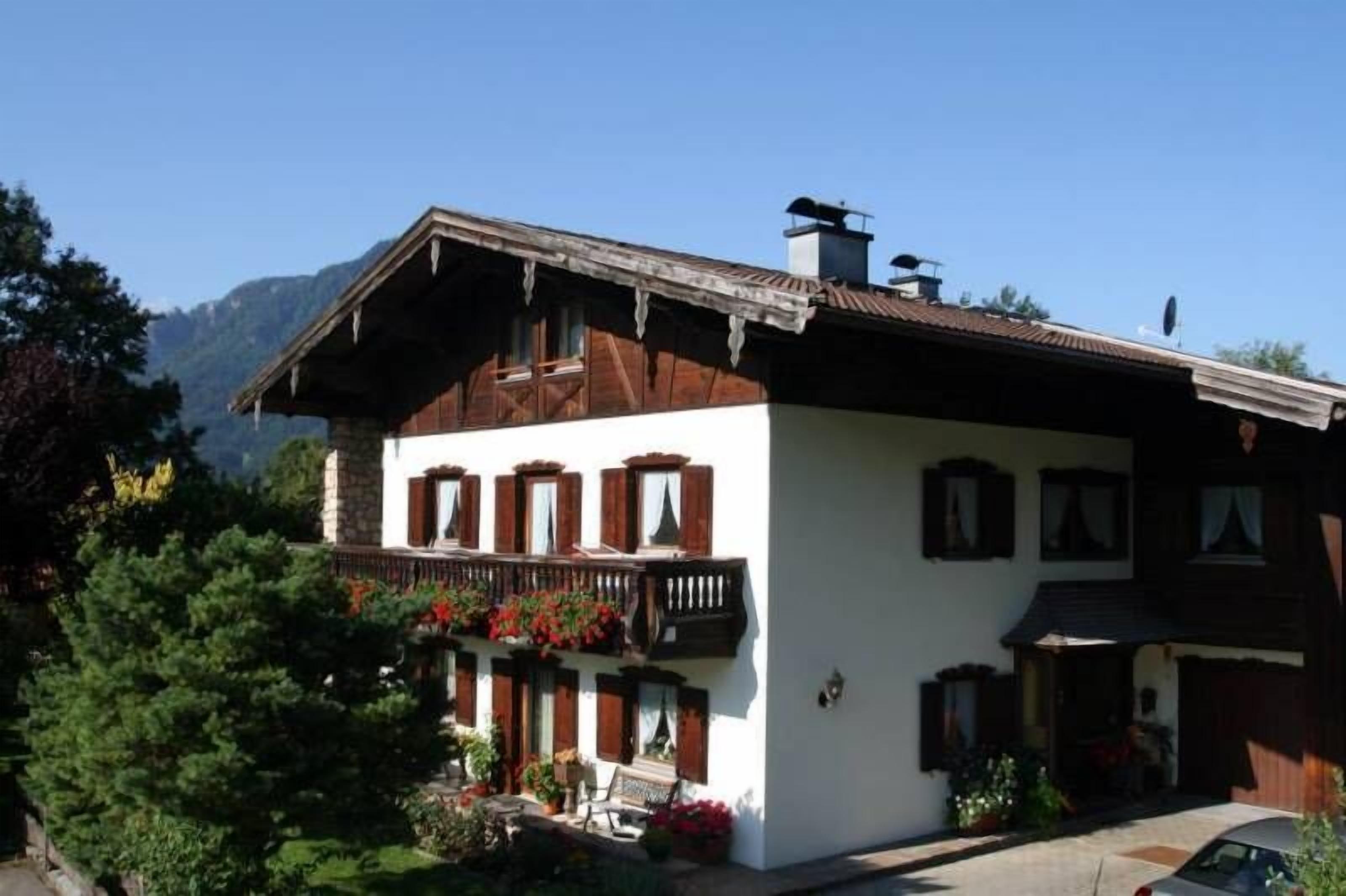 Un chalet traditionnel doté d’un balcon en bois, de murs blancs et surplombant un paysage montagneux.