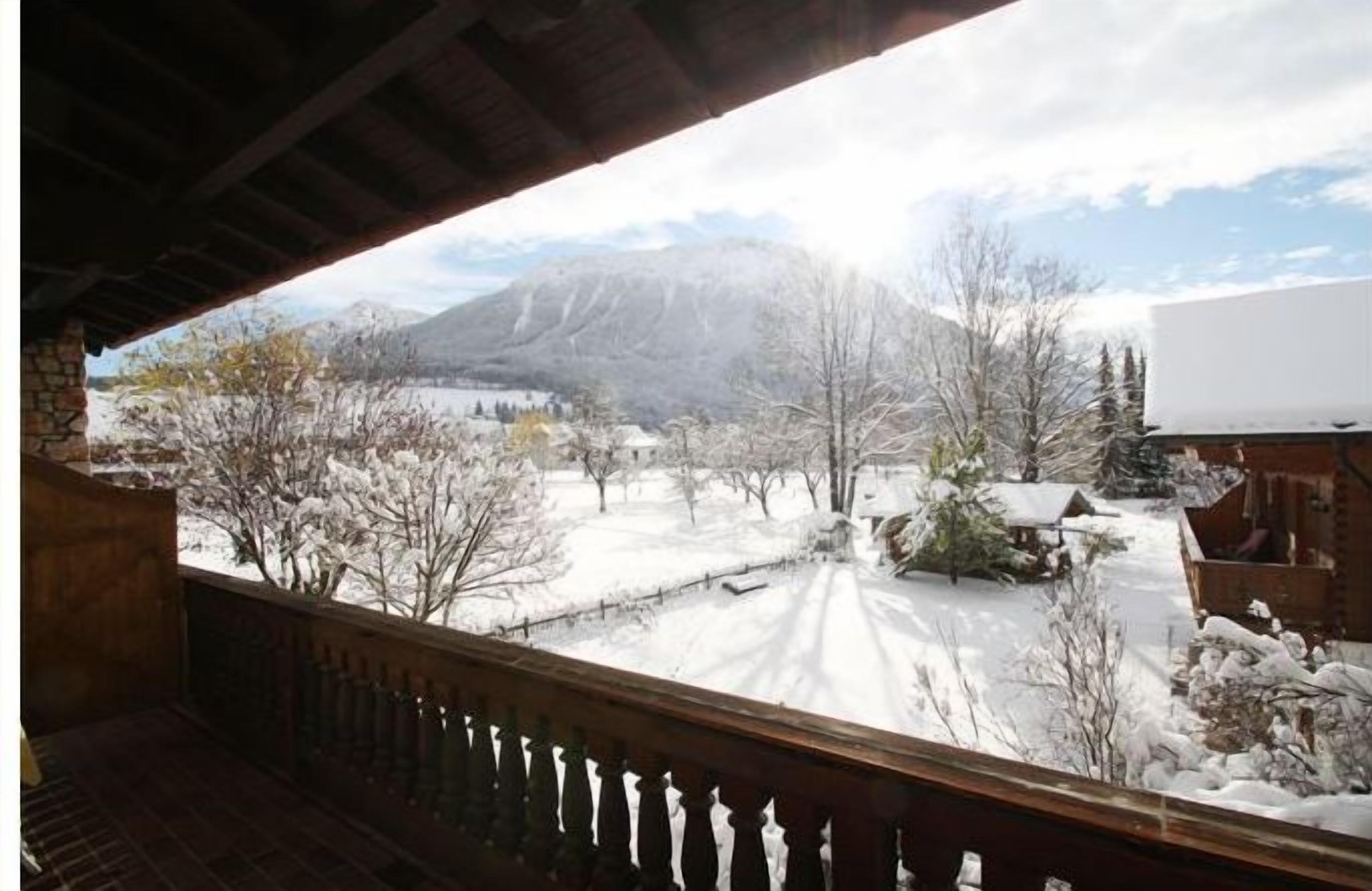 Un paysage enneigé avec des montagnes en arrière-plan, vu depuis un balcon doté d’une balustrade en bois.