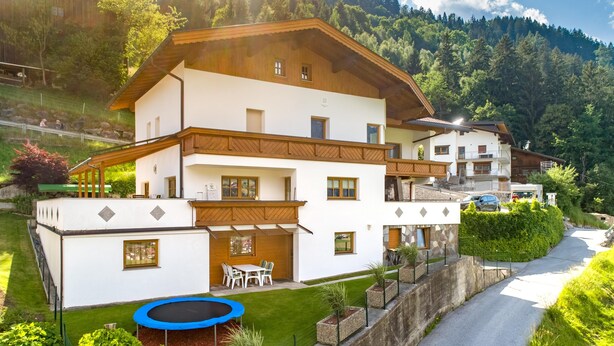 A two-story house with a balcony, a small patio with a table and chairs, and a trampoline in the yard. - Charming holiday home near the ski resort (Kaltenbach)