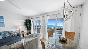 Un salon moderne avec une table à manger en verre, des chaises en osier et une vue sur l’océan.