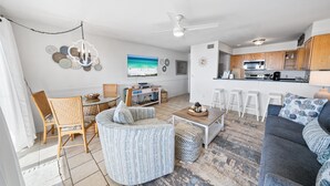 Un salon moderne avec un téléviseur, un coin salon et une cuisine en arrière-plan.