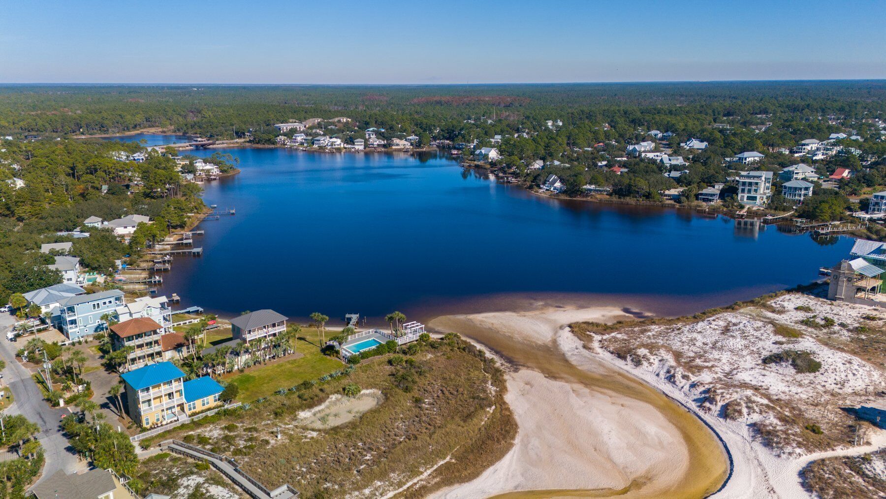 Vue aérienne d’une zone côtière avec un grand lac, des immeubles résidentiels et une plage de sable.