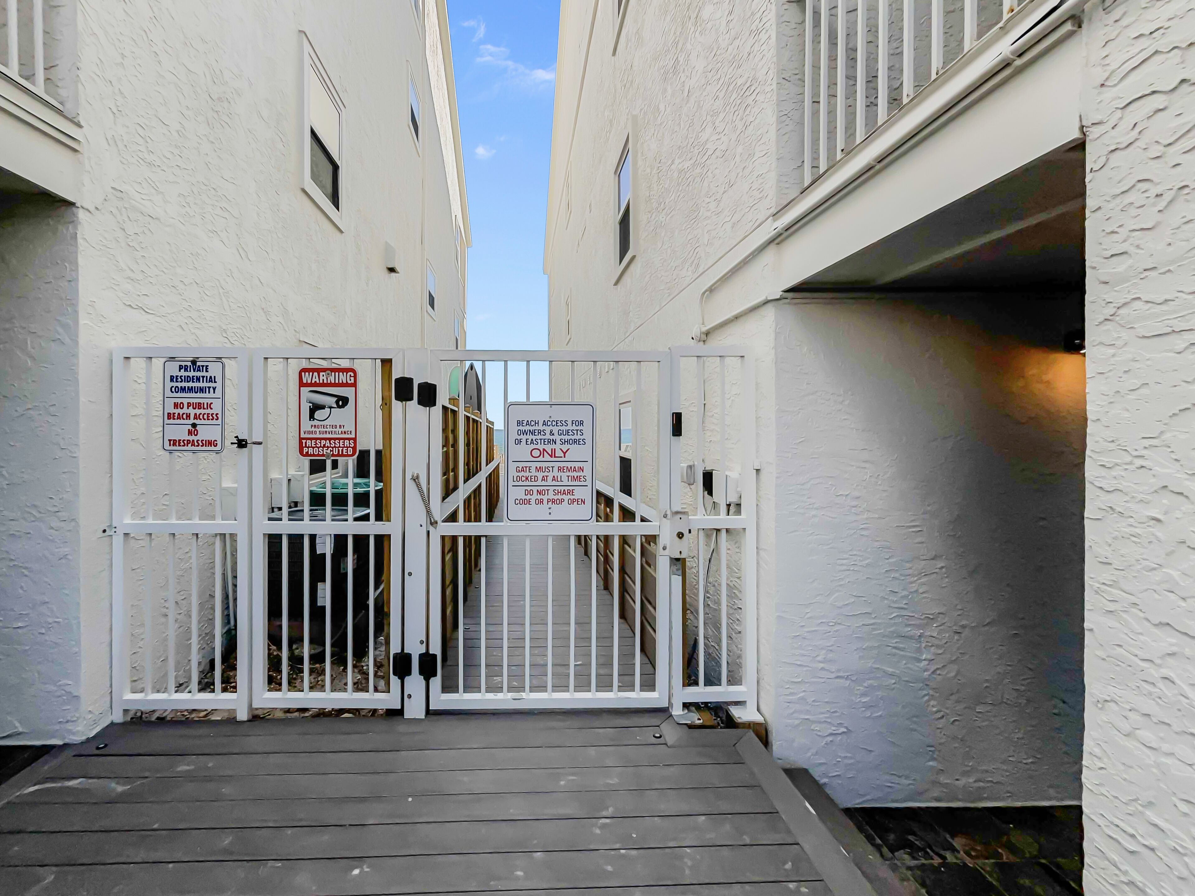 A gated entrance to a private residential community with security measures including a surveillance camera and warning signs.