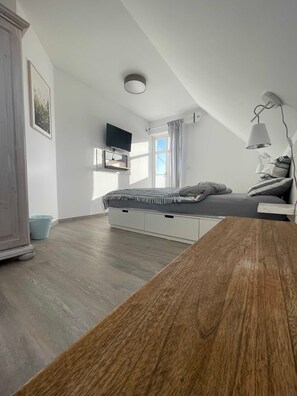 A bedroom with a bed, a TV mounted on the wall, a ceiling light, and a window with curtains.