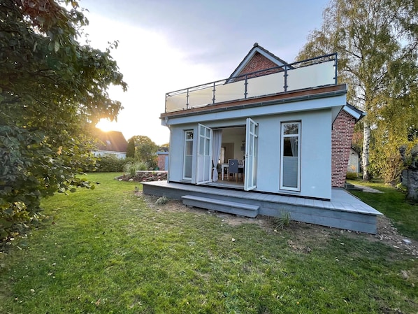 A modern house with a balcony, a small garden, and a clear sky.
