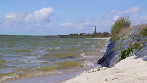 A beach with a lighthouse in the distance, sandy shore, and waves. - Holiday Home in Hindeloopen by Lake (Hindeloopen)