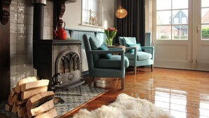 A cozy living room with a fireplace, two teal armchairs, a fluffy rug, and a view of the outside. - Holiday Home in Hindeloopen by Lake (Hindeloopen)