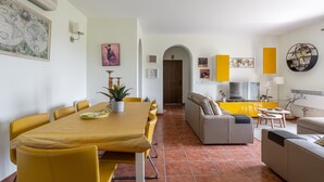 Un coin repas avec une table et des chaises jaunes, un canapé et un téléviseur en arrière-plan.
