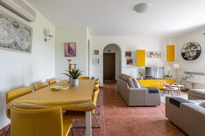 A dining area with a yellow table and chairs, a sofa, and a TV in the background.