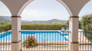 Une piscine avec vue sur les montagnes, une pergola aux colonnes blanches et un espace clos aménagé avec des chaises.